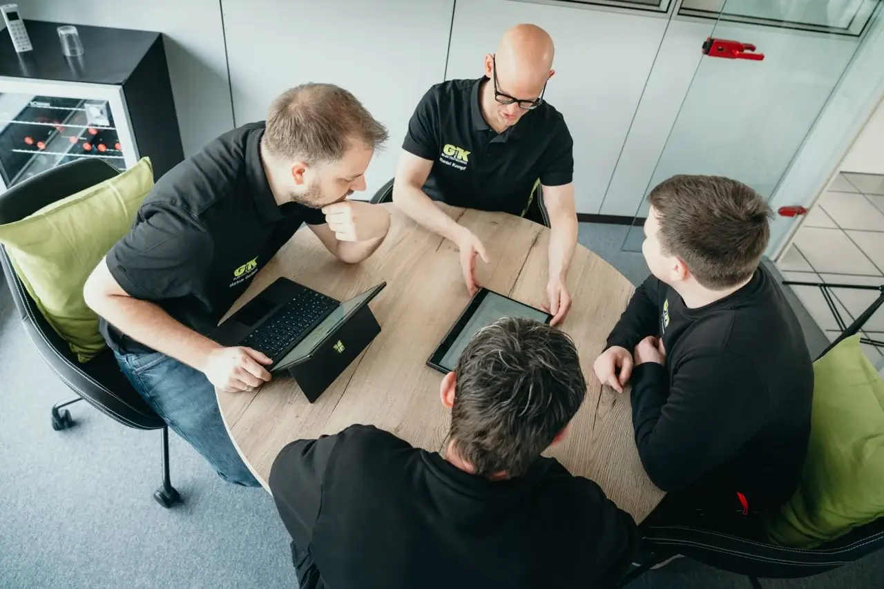 Mitarbeiter von GplusK sitzen gemeinsam am Tisch vor ihren Laptops und bereden die Planung einer PV-Anlage